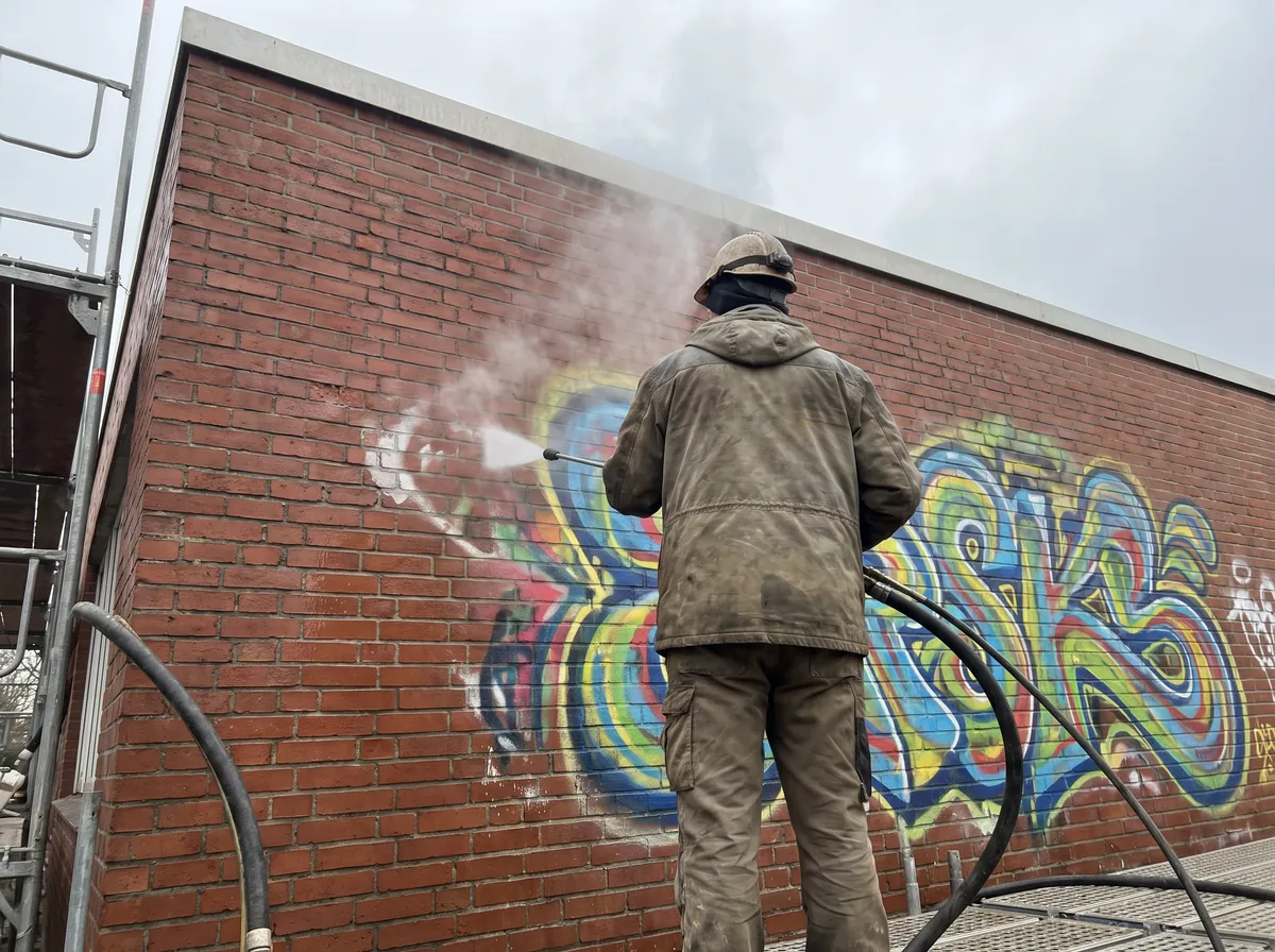 Graffiti wird mit einer Hochdrucklanze von einer Backsteinwand entfernt